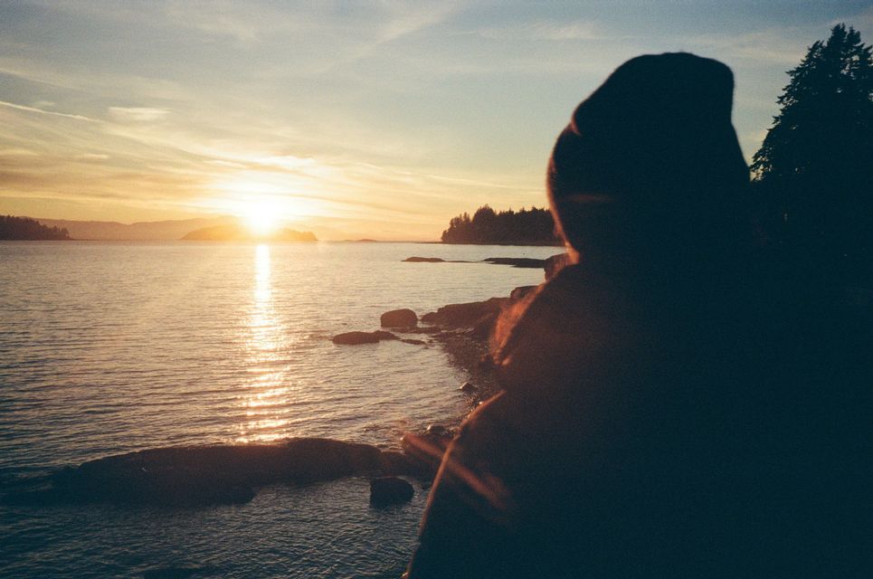 Une silhouette contemple le coucher de soleil se reflétant sur l'eau depuis une côte rocheuse.