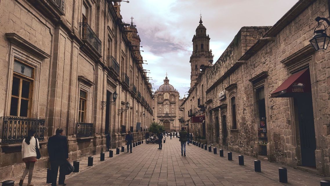 Vista de una calle empedrada flanqueada por edificios históricos, que conduce a una gran catedral con cúpula bajo un cielo nublado.
