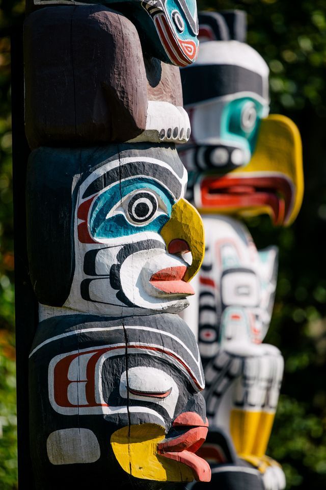 Gros plan sur plusieurs totems en bois sculptés et peints de couleurs vives, alignés en extérieur.