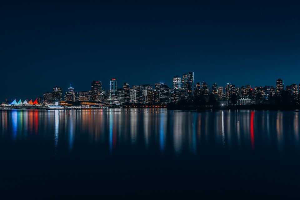 La skyline illuminée d'une ville se reflétant sur un plan d'eau la nuit, avec des lumières colorées sur la surface calme.
