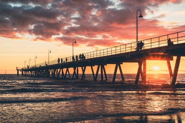Siluetas de personas en un largo muelle sobre el océano durante un atardecer dramático y colorido.