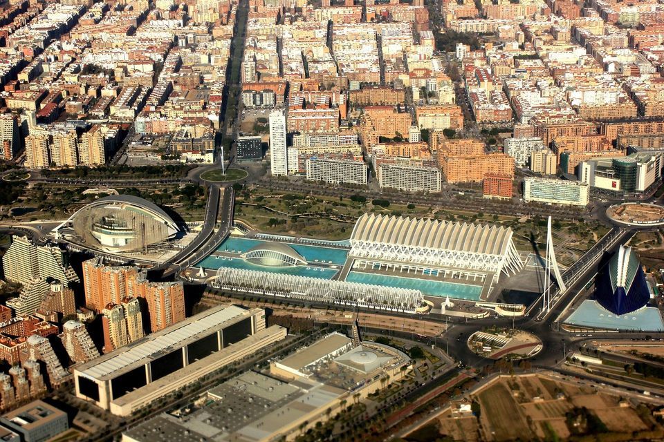 Una vista aérea de un complejo arquitectónico futurista con edificios blancos y piscinas azules, ubicado en un extenso paisaje urbano.