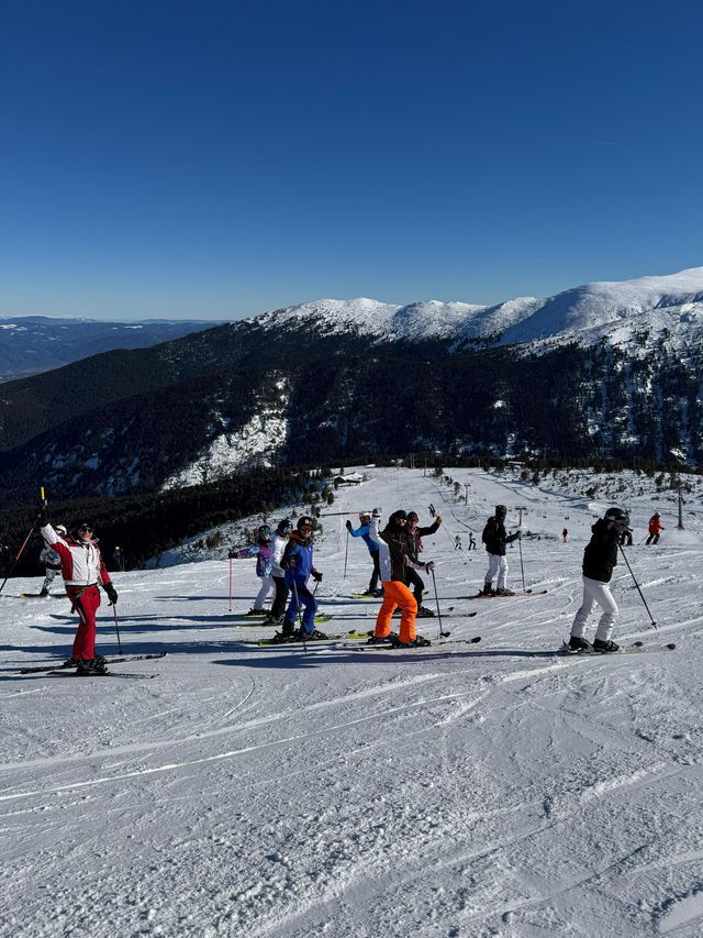 Un viaggio di gruppo WeRoad in tenuta da sci completa, in posa su un pendio montano innevato sotto un cielo azzurro chiaro.