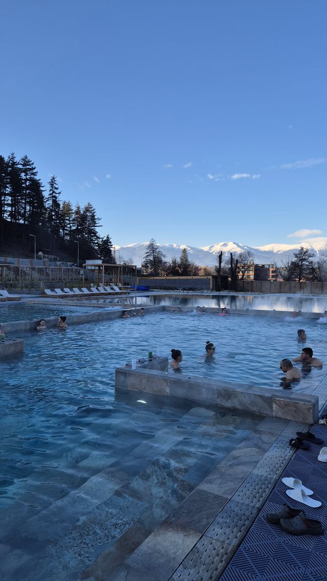 Un viaggio di gruppo WeRoad che si rilassa in una piscina termale all'aperto con vista su montagne innevate sotto un cielo azzurro.