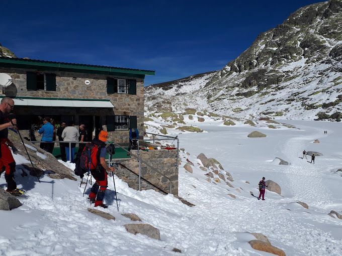 Un viaje en grupo de WeRoad con senderistas en un refugio de montaña de piedra, en un paisaje nevado bajo un cielo azul despejado.