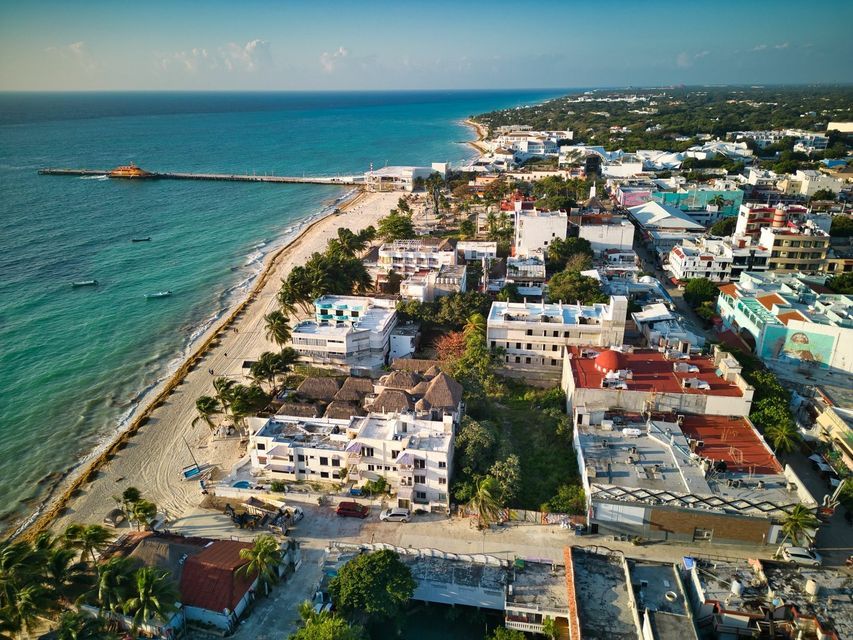 Vue aérienne d'une ville côtière avec une plage de sable et une longue jetée s'avançant dans l'océan turquoise.