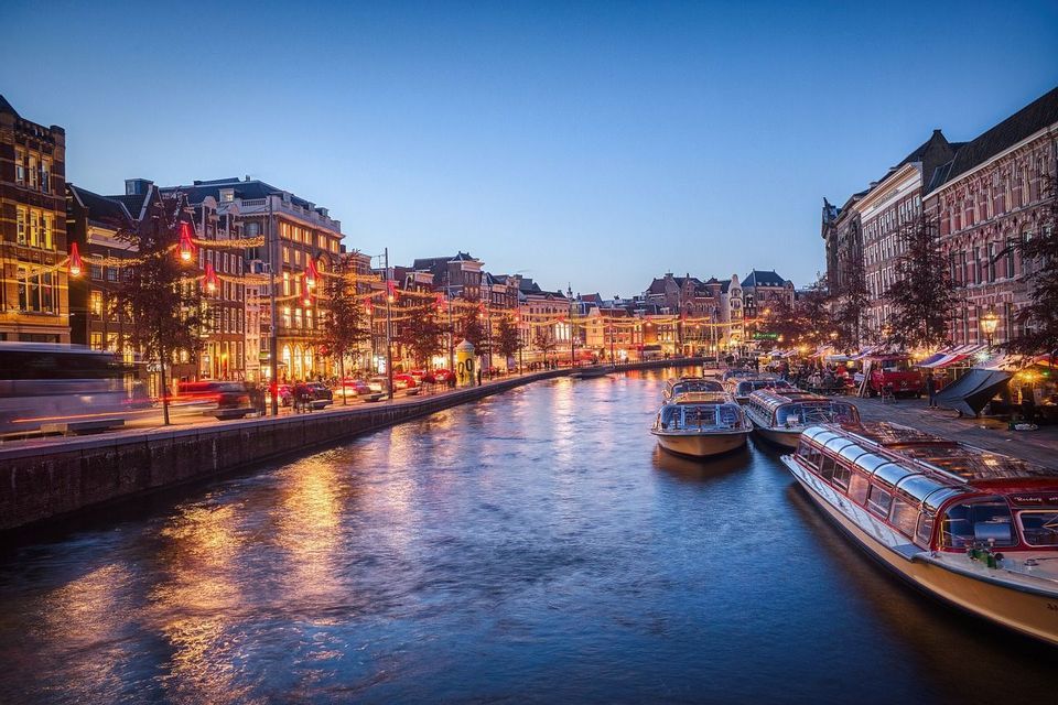 Un canale cittadino al tramonto, con edifici illuminati che si riflettono sull'acqua e barche turistiche ormeggiate lungo le rive.