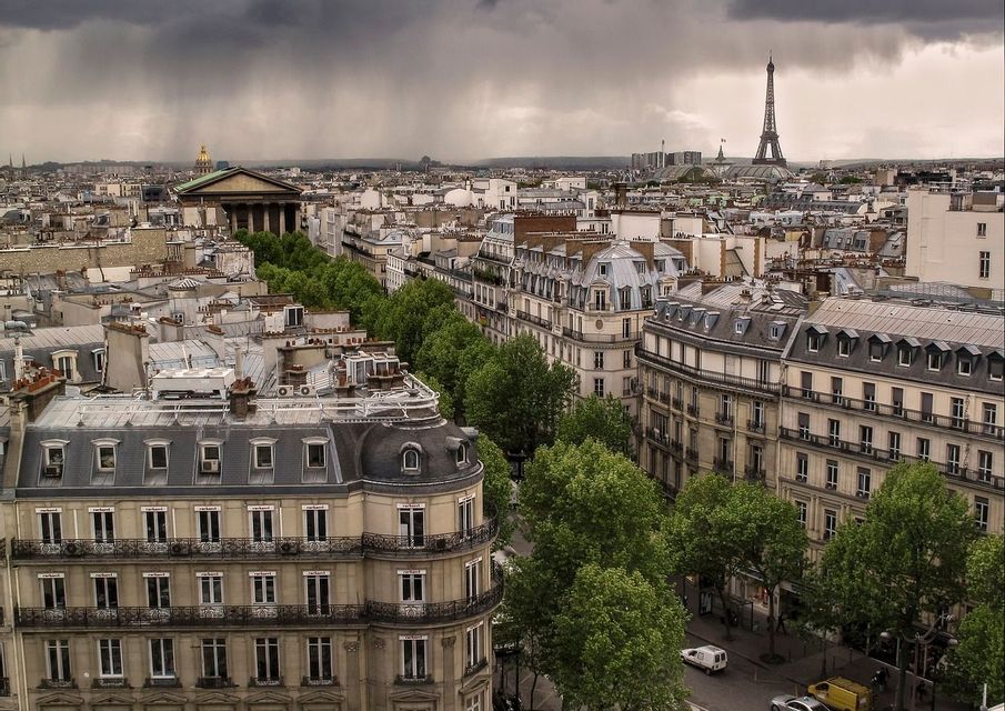 Una vista panoramica sui tetti di Parigi e sulla Torre Eiffel sotto un cielo scuro e tempestoso con la pioggia che cade in lontananza.