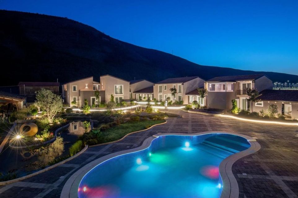 Un resort con edifici illuminati e una piscina colorata di notte, sullo sfondo di una montagna scura