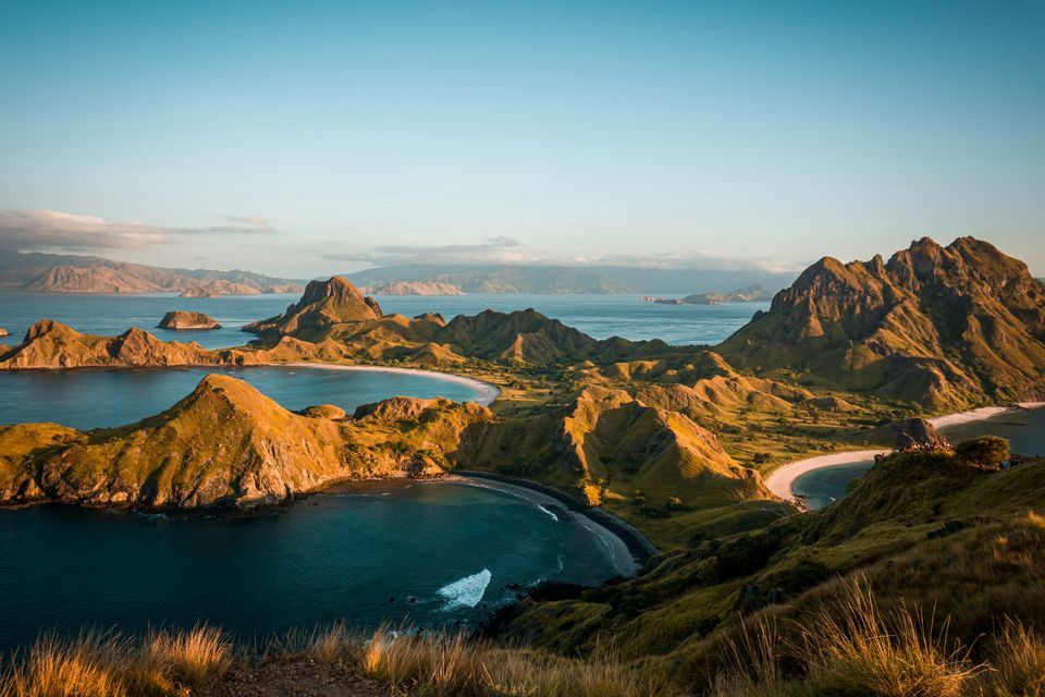 Una vista dall'alto di isole dorate e collinari con calette sabbiose, circondate da acque oceaniche di un blu profondo sotto un cielo limpido.