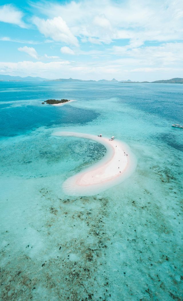 Veduta aerea di un viaggio di gruppo WeRoad su un banco di sabbia rosa a forma di mezzaluna nell'oceano turchese.