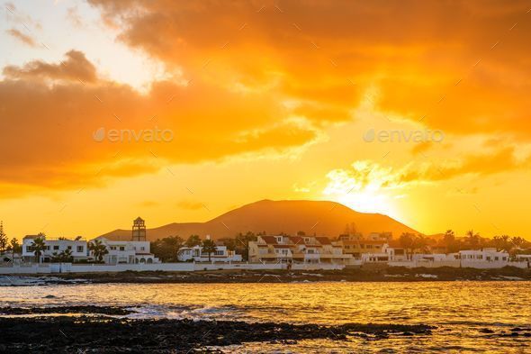 Die Sonne geht hinter einem Berg unter, beleuchtet eine Küstenstadt und spiegelt ein orangefarbenes Glühen auf dem Wasser wider.