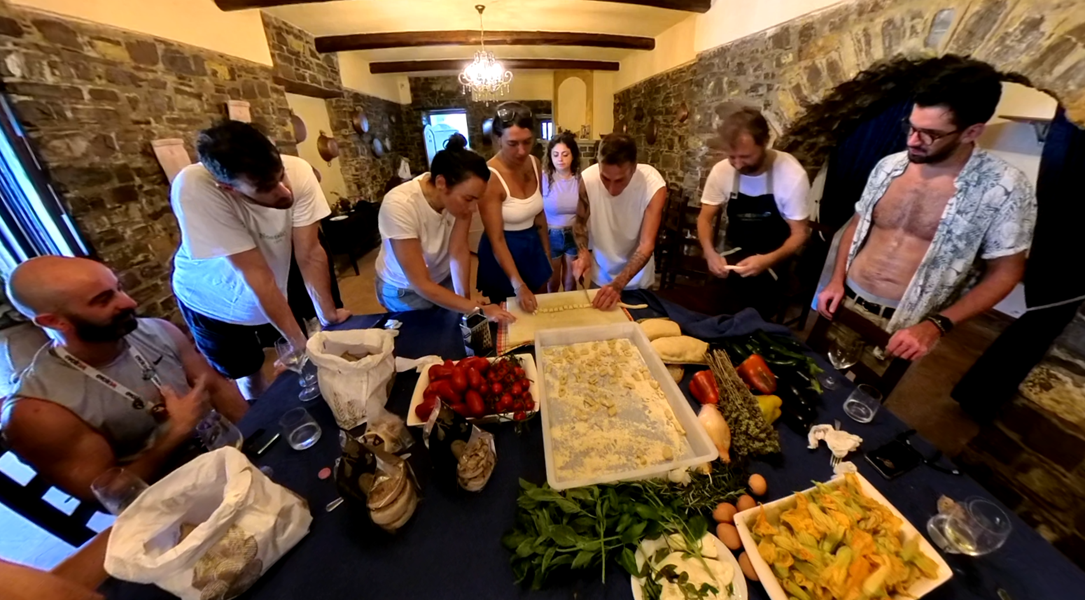 Un viaggio di gruppo WeRoad partecipa a una lezione di cucina, preparando pasta fresca insieme attorno a un tavolo in una cucina rustica.
