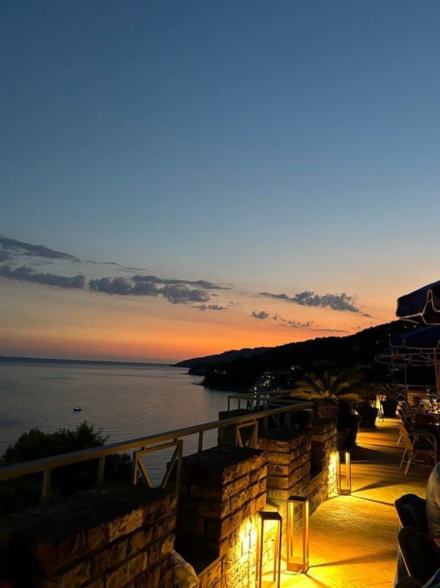 Una vista da una terrazza in pietra illuminata con affaccio sul mare e sulla costa in silhouette al tramonto.