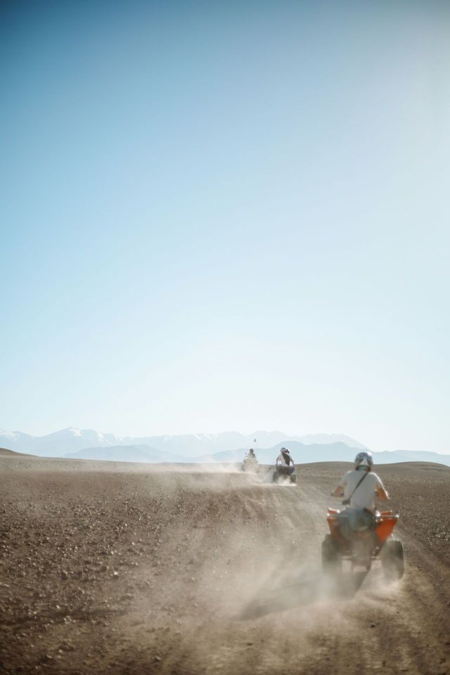 Un viaje en grupo de WeRoad en quads por un camino polvoriento en el desierto, con montañas distantes bajo un cielo azul brillante.