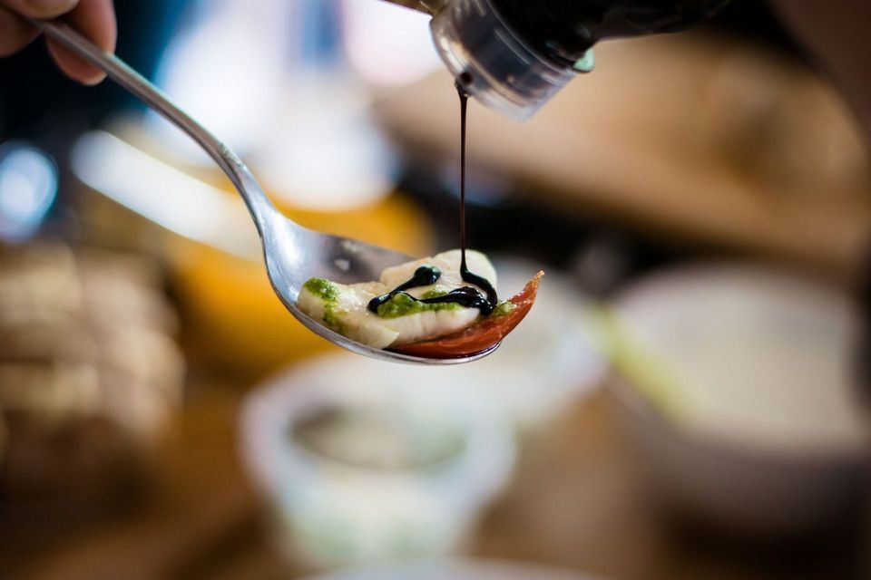 La glassa di aceto balsamico viene versata da una bottiglia su un cucchiaio di mozzarella, pomodoro e pesto.