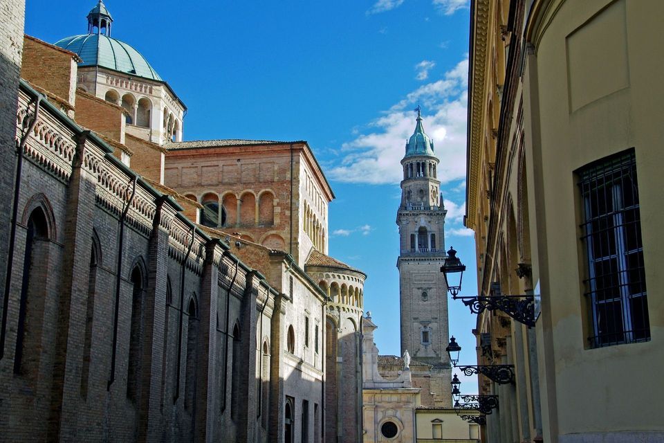 Una storica cattedrale in mattoni e campanile con cupola verde acqua, vista da una strada stretta sotto un cielo azzurro brillante.