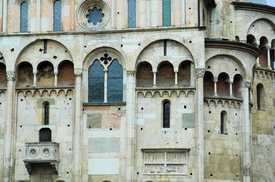 Una vista dettagliata della facciata in pietra di una cattedrale romanica, che mostra finestre ad arco, logge e intagli intricati.