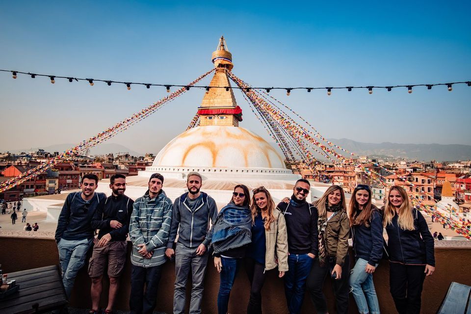 Un groupe WeRoad pose pour une photo sur un toit-terrasse avec un grand stupa blanc et des drapeaux de prière colorés en arrière-plan.