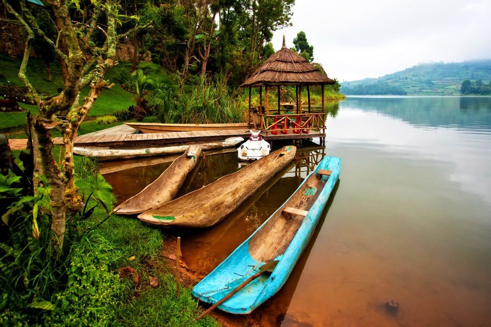 Canoe in legno ormeggiate sulla riva erbosa di un lago calmo con un gazebo dal tetto di paglia su un molo.