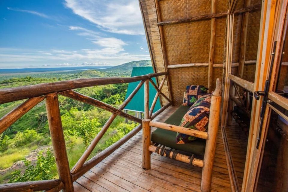 Una panca di legno sul balcone di un rifugio rustico, con vista su un vasto paesaggio verde di colline sotto un cielo parzialmente nuvoloso.