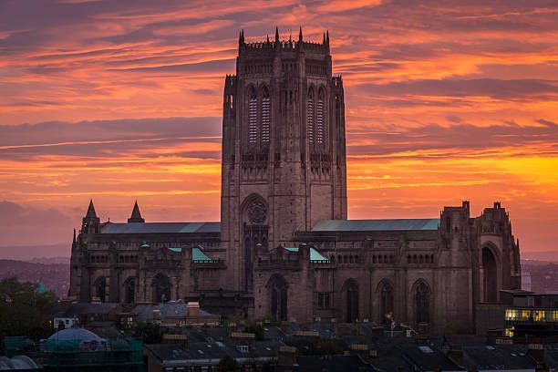 Una cattedrale in stile gotico con una grande torre centrale stagliata contro un cielo striato di nuvole arancioni e viola al tramonto.