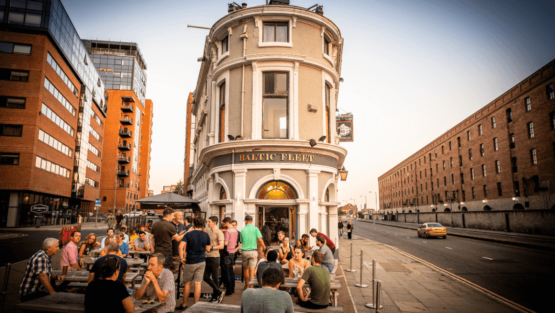 Una folla di persone socializza ai tavoli all'aperto di fronte al pub Baltic Fleet su una via della città.