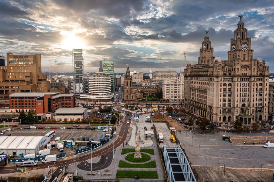 Una vista sopraelevata di uno scenario urbano con una grande torre dell'orologio, edifici moderni e strade sottostanti, sotto un cielo drammatico e nuvoloso.