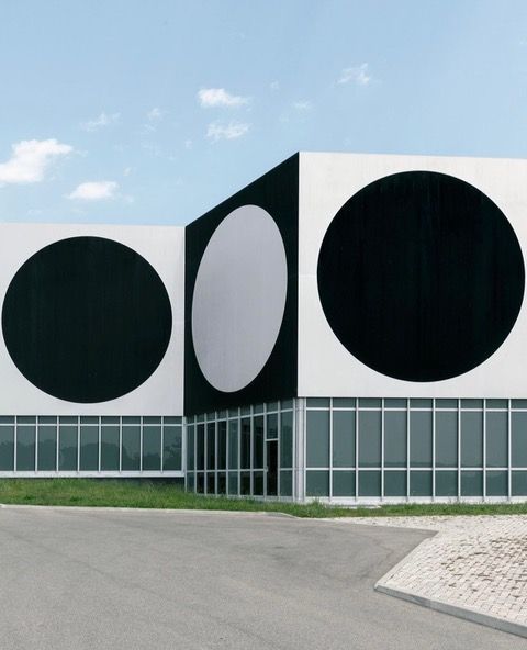 La facciata di un edificio moderno con un motivo grafico di grandi cerchi bianchi e neri sopra una parete finestrata al piano terra.