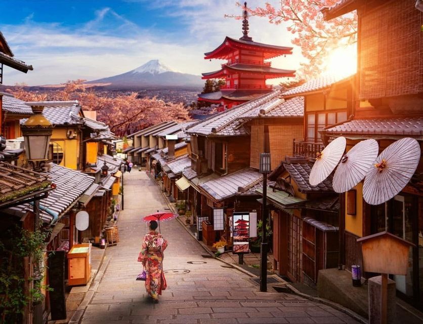 Una mujer en kimono con un paraguas rojo camina por una calle tradicional con una pagoda roja y una montaña nevada al fondo.