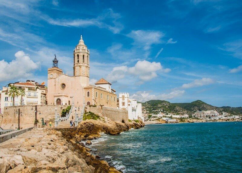 Una grande chiesa con un campanile sorge su una costa rocciosa accanto al mare blu sotto un cielo parzialmente nuvoloso