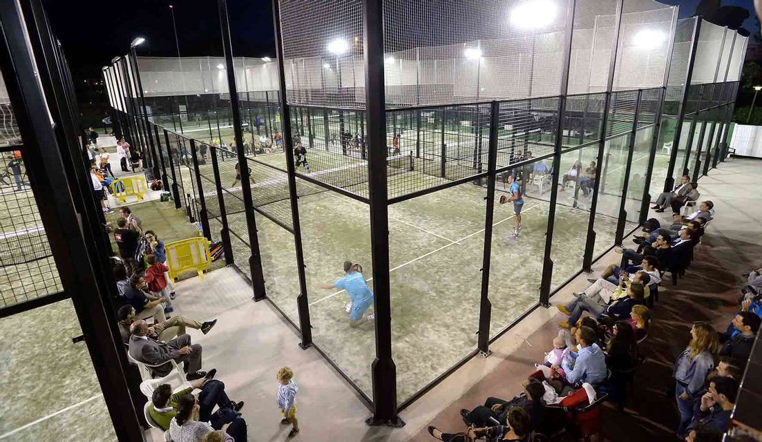 Si gioca una partita di padel su un campo illuminato di notte, con spettatori a bordo campo.