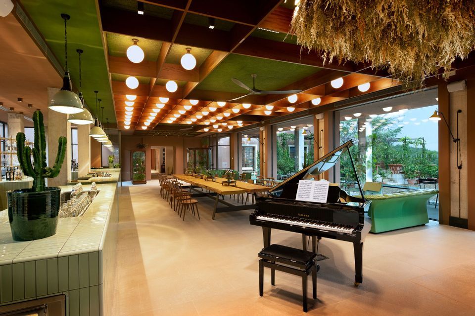Interno di una stanza moderna e spaziosa con un pianoforte a coda, una lunga zona pranzo e un bancone piastrellato sotto un soffitto a cassettoni.