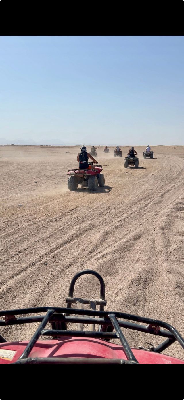 Un viaggio di gruppo WeRoad con quad in fila attraverso un vasto deserto, visto in prima persona.