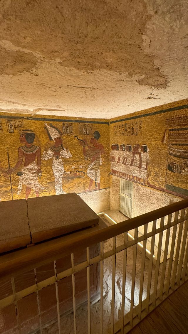 Vista da una passerella all'interno di un'antica tomba egizia, che mostra un sarcofago di pietra e pareti coperte da geroglifici dipinti.