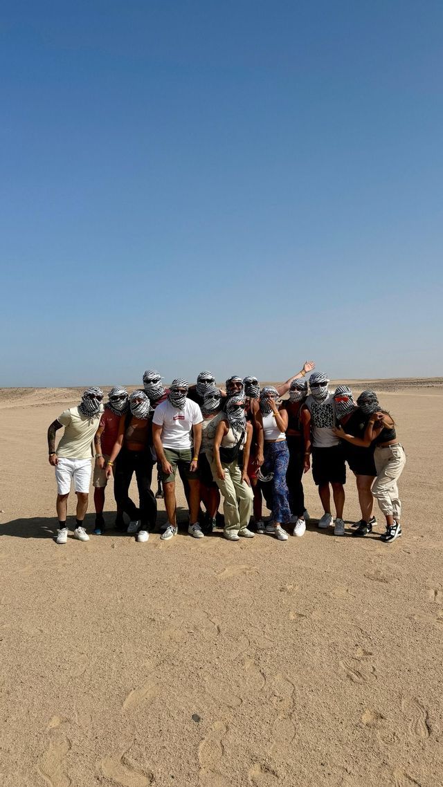 Un gruppo WeRoad posa insieme nel deserto, indossando foulard coordinati a fantasia bianco e nero e occhiali da sole.