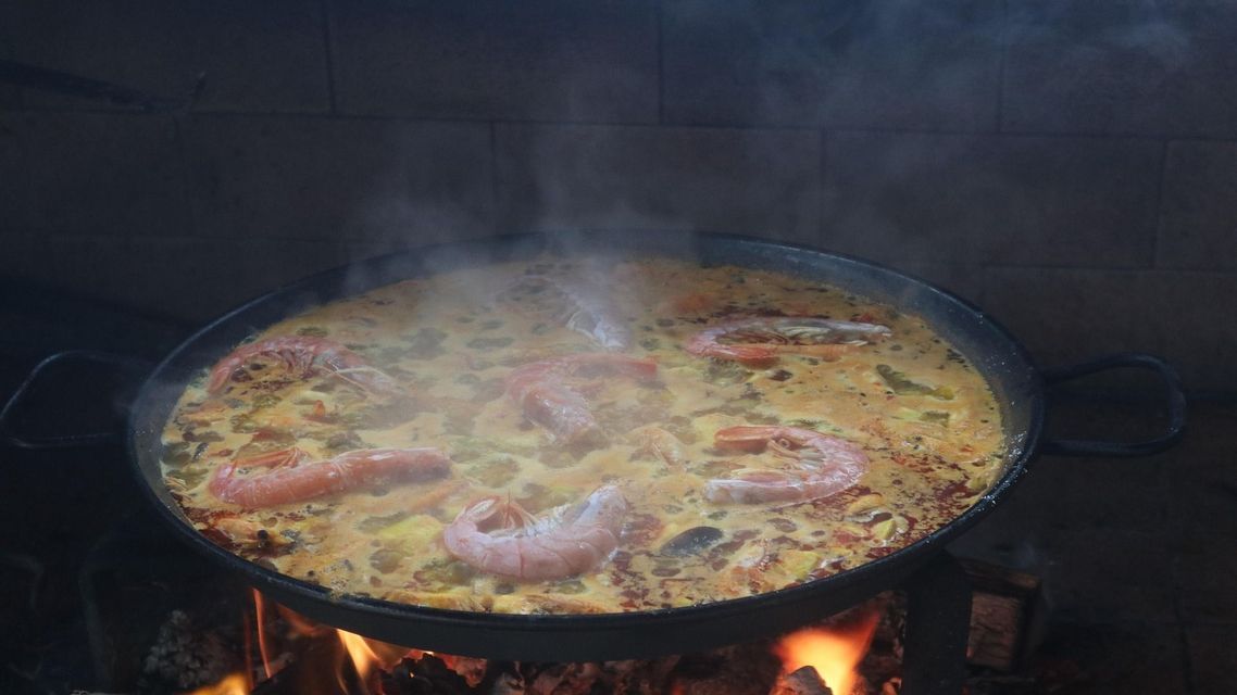 Una grande padella di paella ai frutti di mare con gamberi, fumante mentre cuoce su un fuoco a legna.