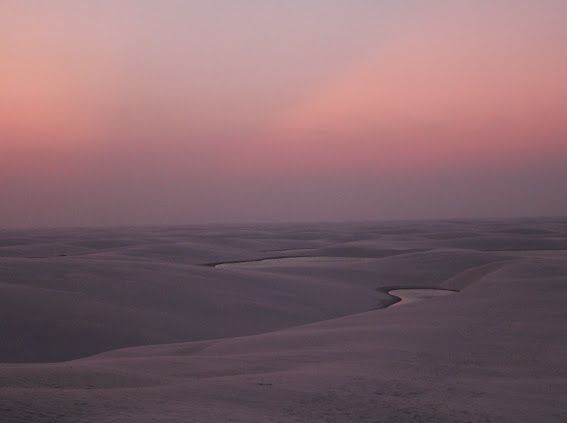 Dune di sabbia bianca e lagune sinuose attraverso un vasto paesaggio desertico sotto un cielo rosa al tramonto.