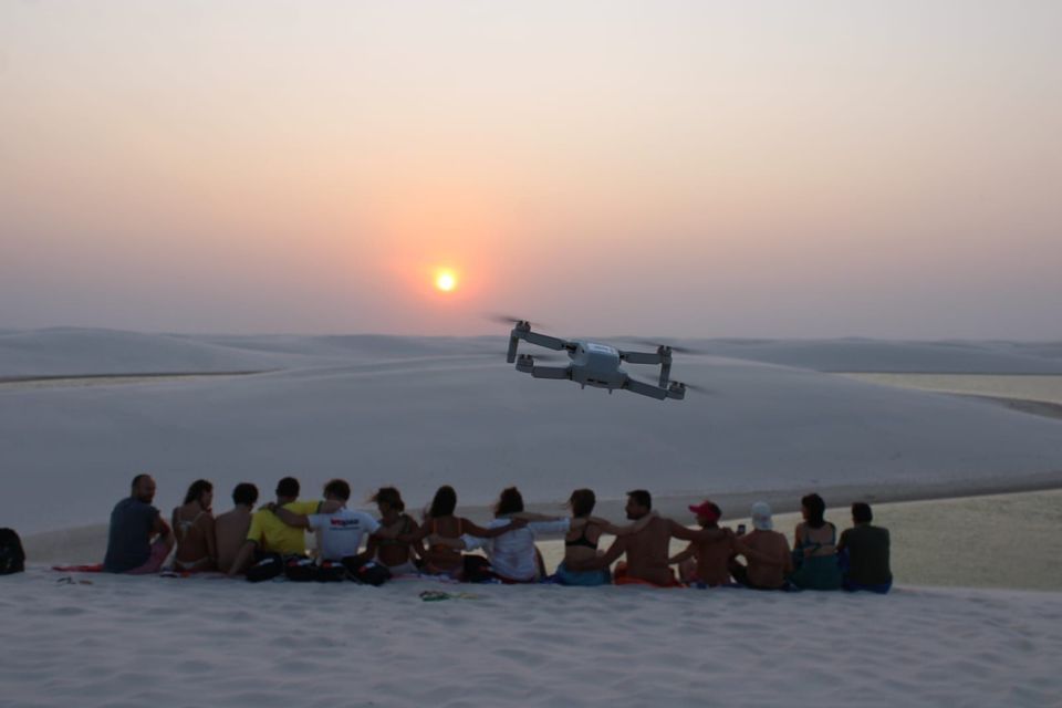 Un drone immortala un gruppo WeRoad seduto su dune di sabbia bianca al tramonto.