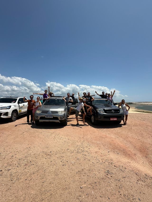 Un viaggio di gruppo WeRoad in posa per una foto su e intorno a tre veicoli 4x4 su una strada sterrata sotto un cielo azzurro brillante.