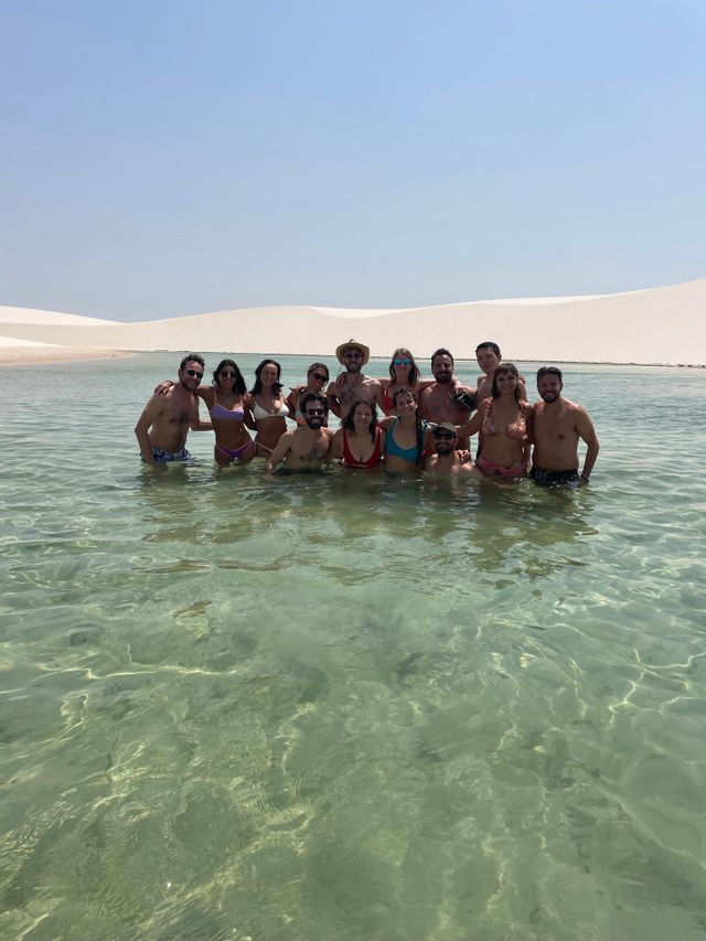 Un viaggio di gruppo WeRoad in posa insieme nell'acqua cristallina di una laguna con dune di sabbia bianca sullo sfondo.