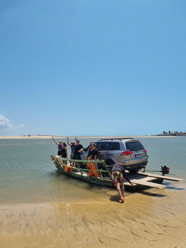 Un viaggio di gruppo WeRoad su un piccolo traghetto con un SUV arriva su una spiaggia sabbiosa sotto un cielo azzurro.