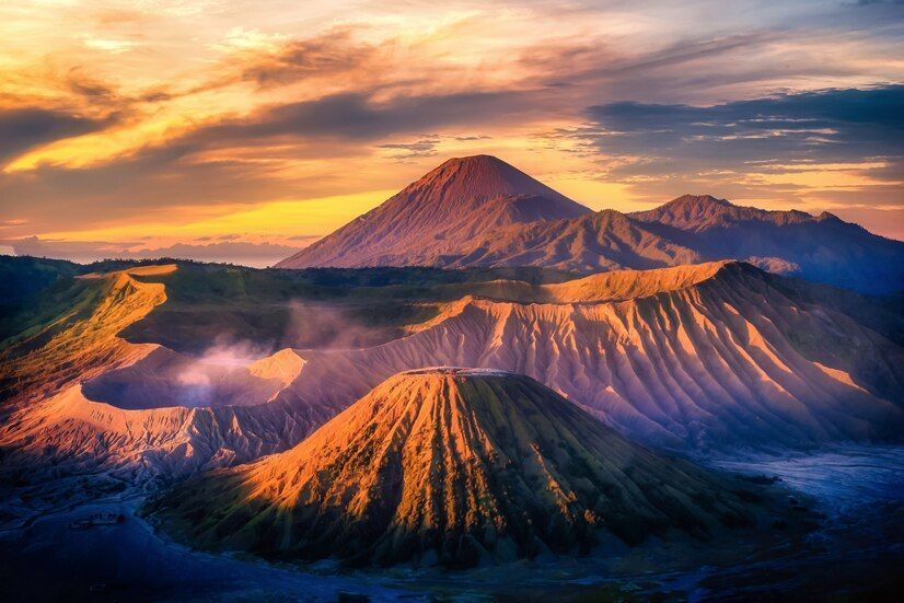 Un paisaje de cráteres volcánicos y montañas iluminado por un amanecer dorado, con humo saliendo de un cráter.