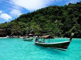 Dos botes de cola larga de madera flotan en agua turquesa junto a una isla exuberante y arbolada bajo un cielo parcialmente nublado.