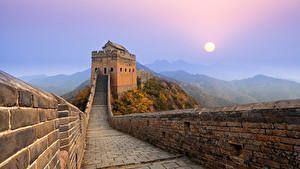 La Gran Muralla China serpentea a lo largo de una cresta montañosa hacia una atalaya mientras el sol sale en un cielo brumoso.