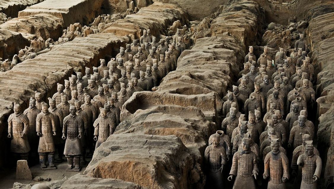 Una colección de estatuas de guerreros de terracota se alza en formación dentro de las trincheras de tierra excavadas.
