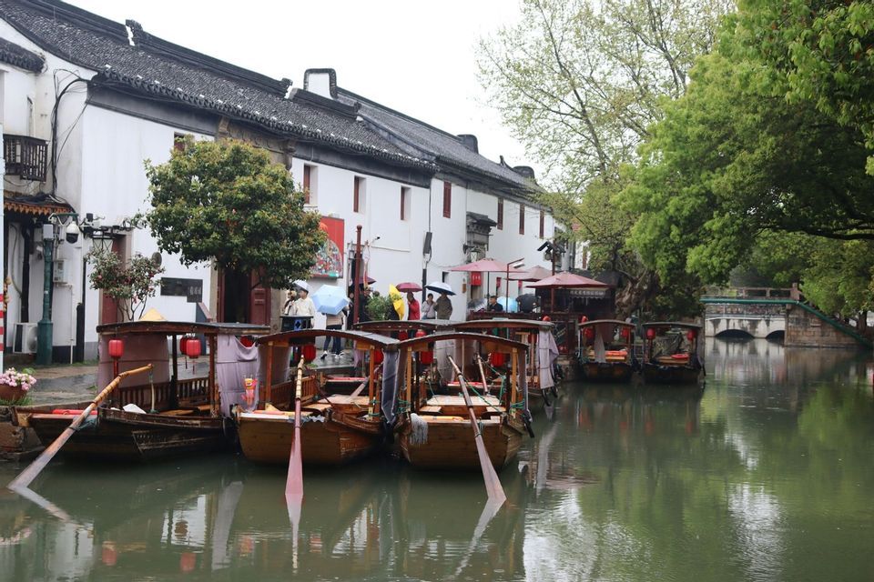 Barcos de madera tradicionales están amarrados en un canal junto a edificios históricos de paredes blancas y árboles frondosos.