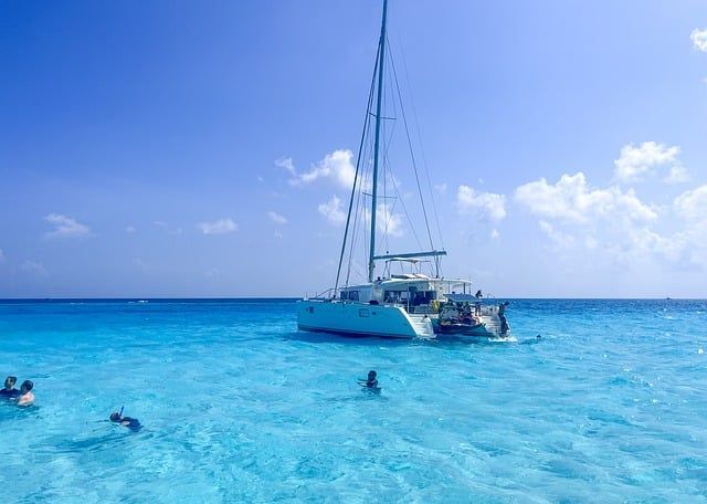 Eine WeRoad Gruppenreise beim Schnorcheln und Schwimmen im klaren türkisfarbenen Wasser neben einem Katamaran unter blauem Himmel.