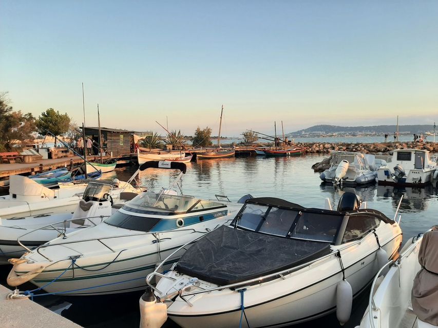 Divers bateaux à moteur et voiliers traditionnels sont amarrés dans un port calme au crépuscule, avec une jetée en bois en arrière-plan.
