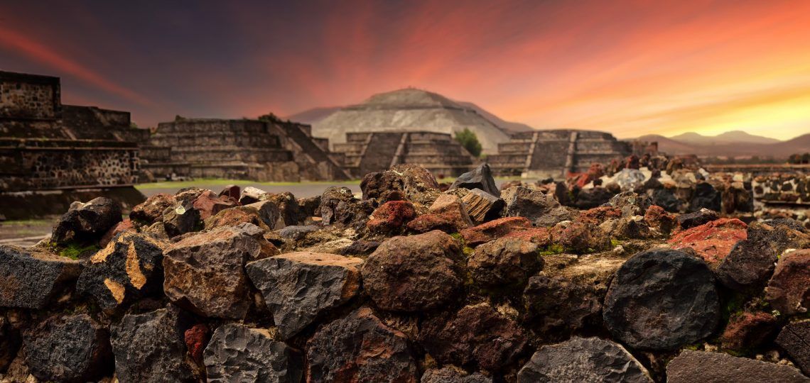 Ancient stone pyramids seen over a rough rock wall during a colorful sunset.